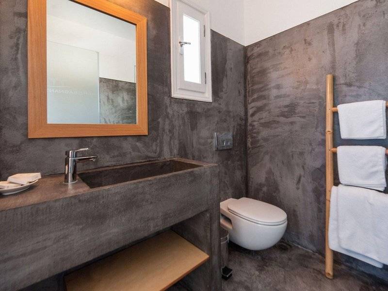 Badezimmer im Paros Agnanti Resort & Spa mit grauen Wänden, einem Waschbecken, einer Toilette und Handtüchern.