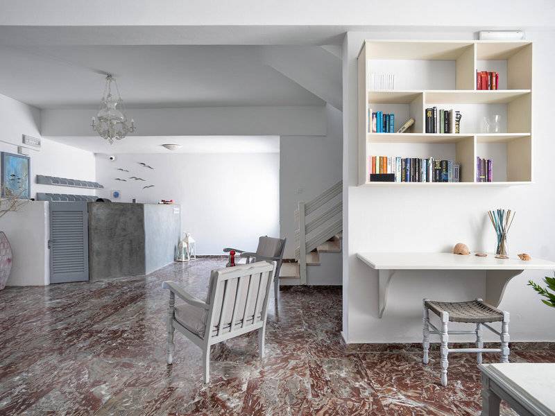 Innenbereich des Iris Boutique Hotel mit Marmorboden, weißen Möbeln, Bücherregal und Treppe.