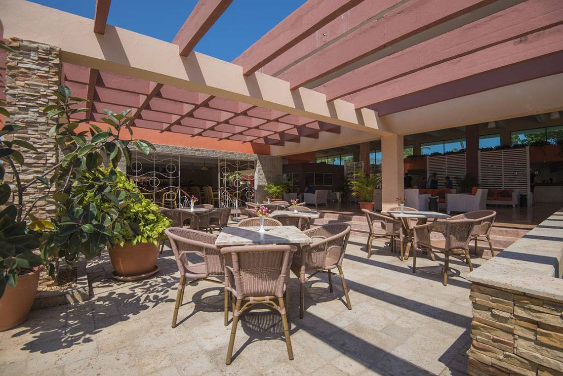 Außenterrasse des Gran Caribe Villa Tortuga Hotels mit Tischen, Stühlen und Pflanzen.