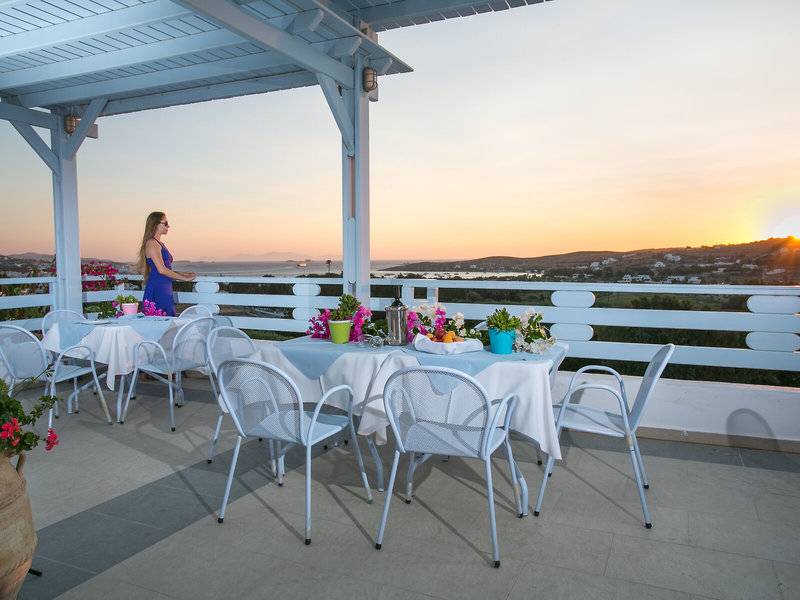Terrasse des Pyrgaki Hotels mit Blick auf den Sonnenuntergang und mehreren gedeckten Tischen.