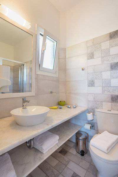 Badezimmer im Pyrgaki Hotel mit Marmorwaschtisch, Spiegel, Fenster und Toilette.