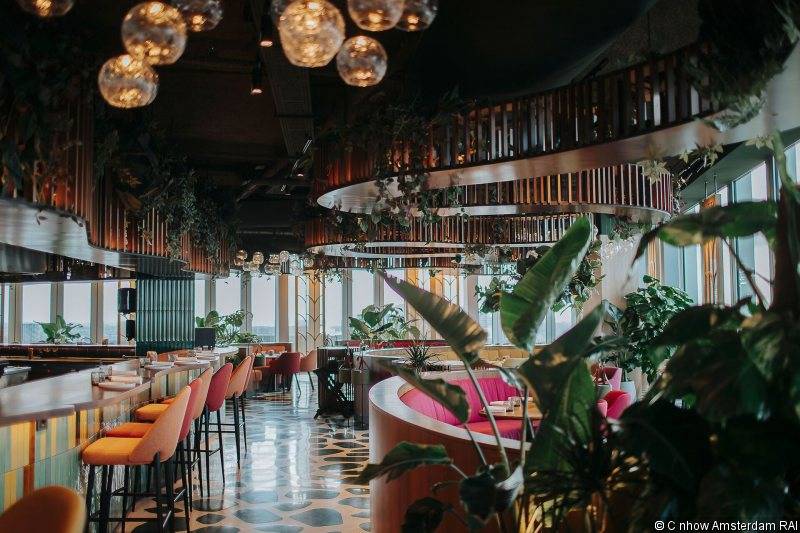Innenansicht des Restaurants im nhow Amsterdam RAI mit hängenden Pflanzen und modernen Möbeln.