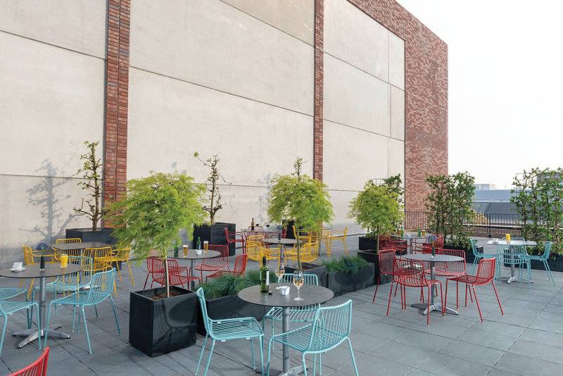 Dachterrasse des Leonardo Royal Hotel Amsterdam mit farbenfrohen Tischen und Stühlen.