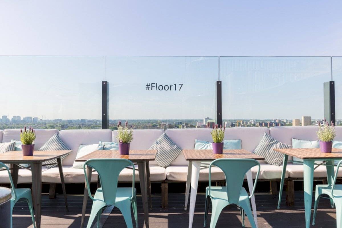 Terrasse im Leonardo Hotel Amsterdam Rembrandtpark mit Tischen, Stühlen und Pflanzen.
