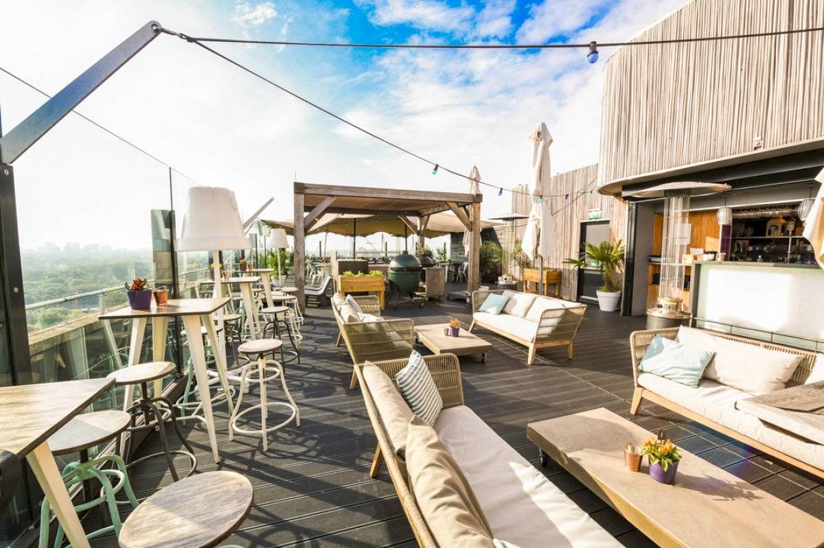 Dachterrasse des Leonardo Hotel Amsterdam Rembrandtpark mit Tischen und Stühlen.