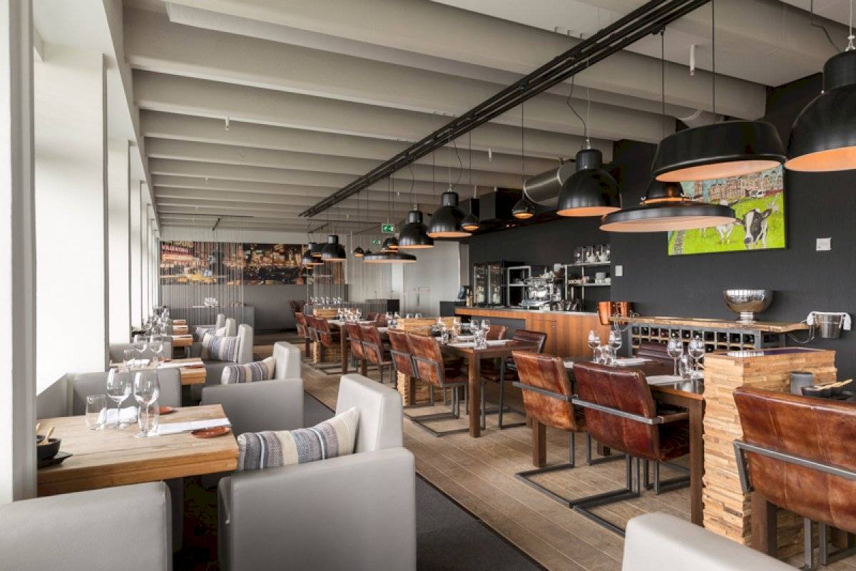 Innenbereich des Leonardo Hotel Amsterdam Rembrandtpark mit Esstischen, Stühlen und Bar.
