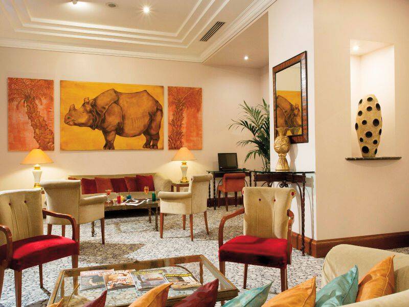 Wohnbereich des Dei Mellini Hotels mit Sofa, Sesseln, Gemälden und einem Tisch.
