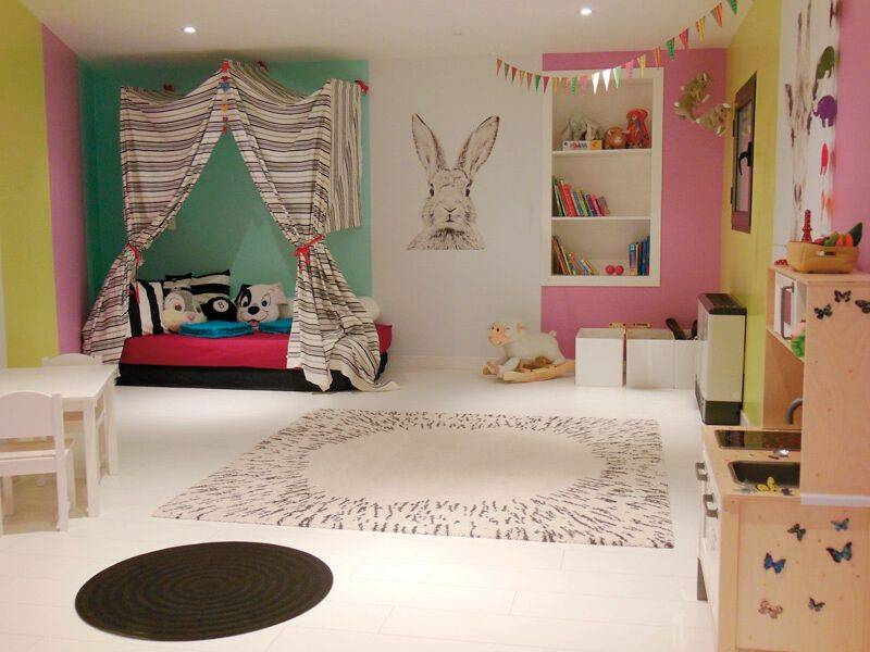 Ein buntes Kinderzimmer mit einem Bett, einem großen Teppich und Spielzeug.