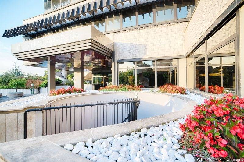 Vorderansicht des NH Roma Villa Carpegna Hotels mit gepflastertem Eingang und roten Blumen