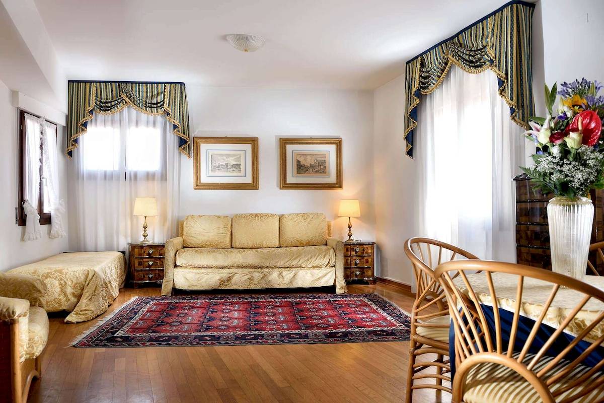 Wohnzimmer im San Marco Palace Hotel mit Sofa, Teppich, Esstisch und Blumenvase.
