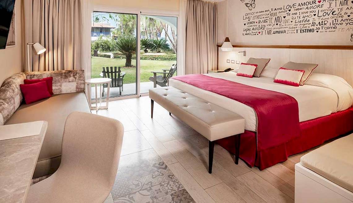 Hotelzimmer im Catalonia Bayahibe mit Blick auf den Garten, großem Bett, Sitzbereich und offenem Balkon.