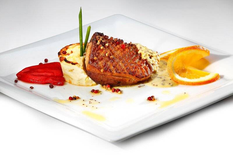 Gebratenes Filetstück auf einem weißen Teller mit Beilagen wie Kartoffelpüree, Paprika und Orangenscheiben.
