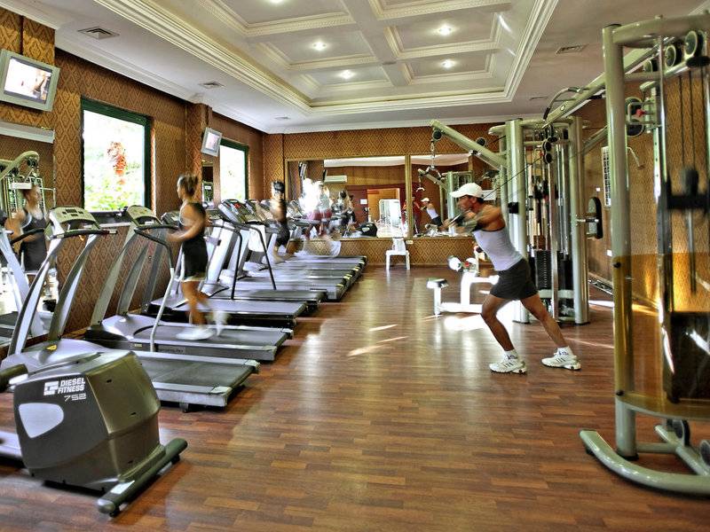 Fitnesscenter im Delphin Deluxe Hotel mit Läufern auf Laufbändern und einem Mann, der an einem Zugapparat arbeitet.