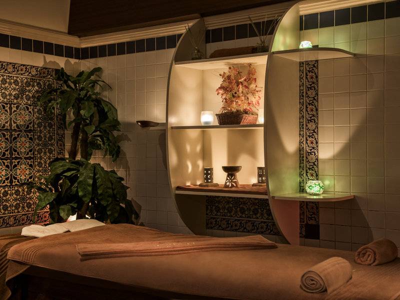 Spa Behandlungsraum im Delphin Deluxe Hotel mit Massageliege, Pflanzen und dekorativen Elementen.