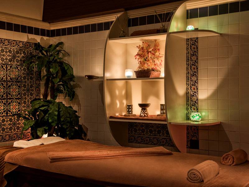 Spa-Behandlungsraum im Delphin Deluxe Hotel mit einem Massagetisch, Pflanzen und dekorativen Elementen.