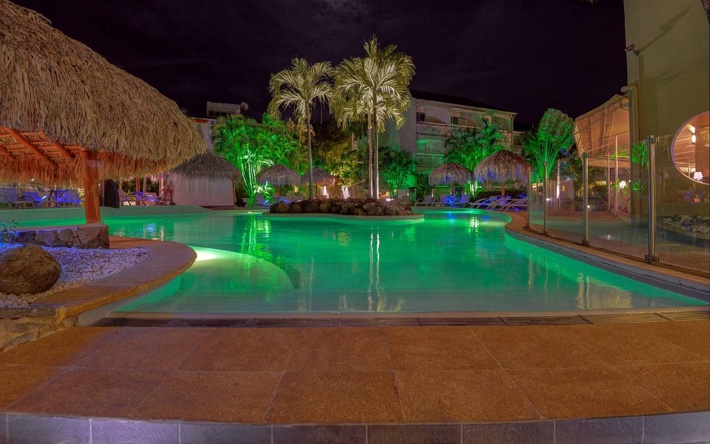 Pool im La Pagerie - Tropical Garden Hotel bei Nacht mit grünen Lichtern und Palmen.