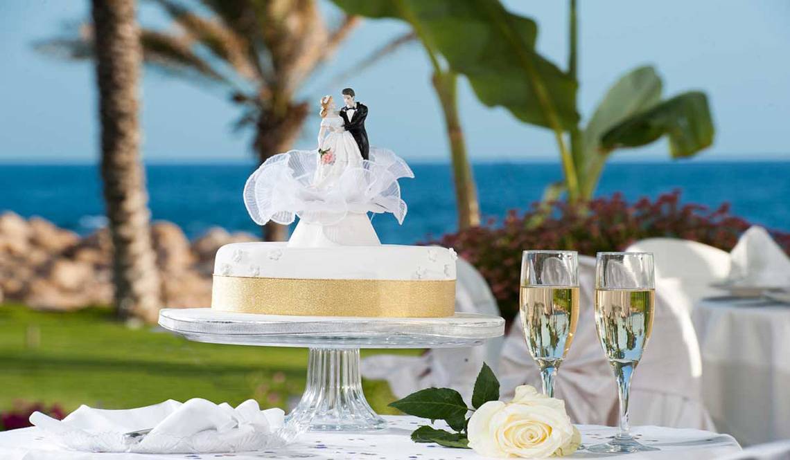 Hochzeitstorte mit Brautpaar-Figuren auf einem Tisch am Strand mit Meerblick