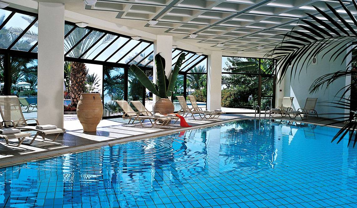 Der Poolbereich des Constantinou Bros Athena Beach Hotels mit Sonnenliegen und Pflanzen.