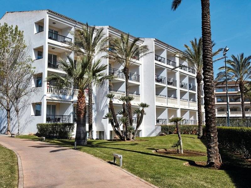 Weißes Apartmentgebäude Beach Club Font de Sa Cala mit Balkonen und Palmen davor