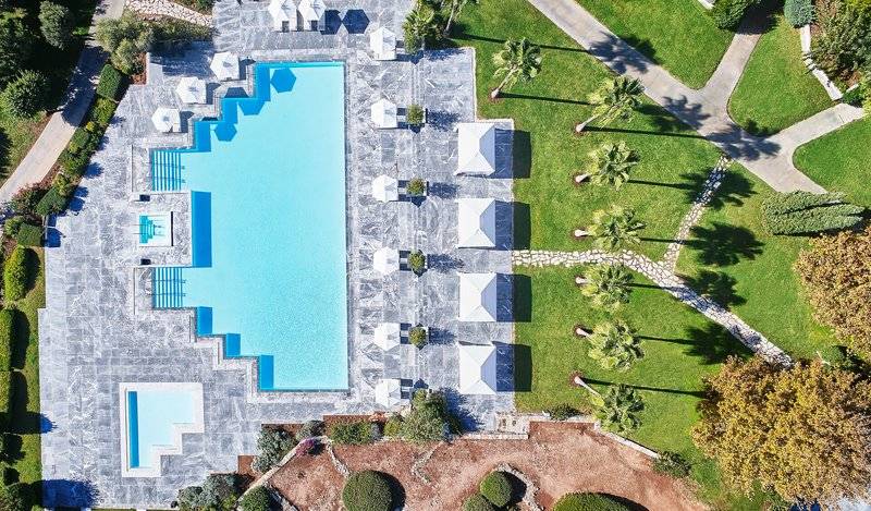 Luftaufnahme des Swimmingpools im Cape Sounio Grecotel Resort mit umliegenden Sonnenschirmen und Rasen.