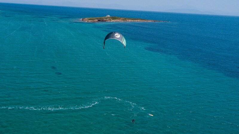 Ein Segelparaglider fliegt über dem blauen Meer mit einer kleinen Insel im Hintergrund.