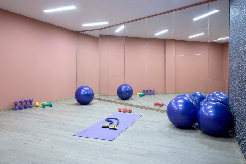 Fitnessraum im Hotel Dolce Athens Attica Riviera mit Spiegelwänden, blauen Gymnastikbällen und Trainingsgeräten.