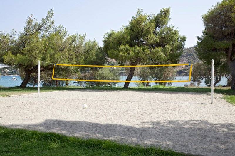 Strandvolleyballnetz mit Ball auf sandigem Boden mit Bäumen und Wasser im Hintergrund