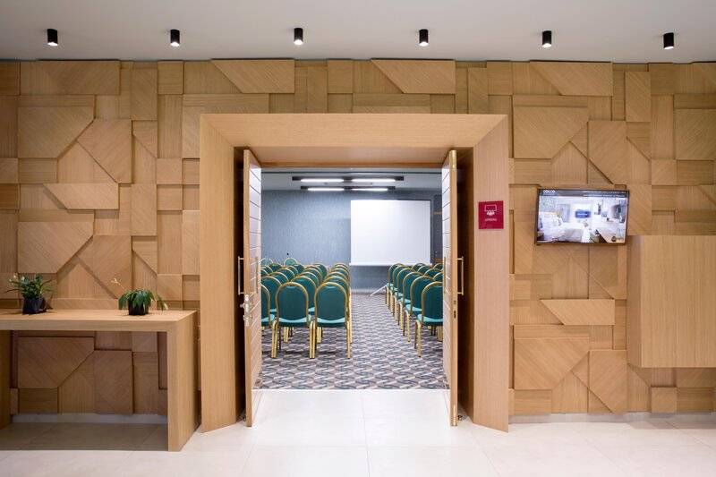 Konferenzraum im Dolce Athens Attica Riviera Hotel mit Holzwänden und grünen Stühlen.