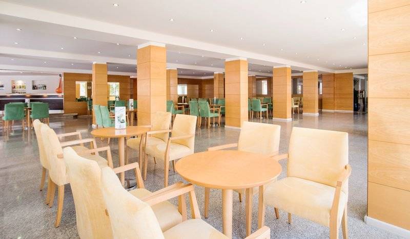 Innenbereich des La Santa Maria Playa Hotels mit hellen Holzmöbeln und grünen Stühlen.