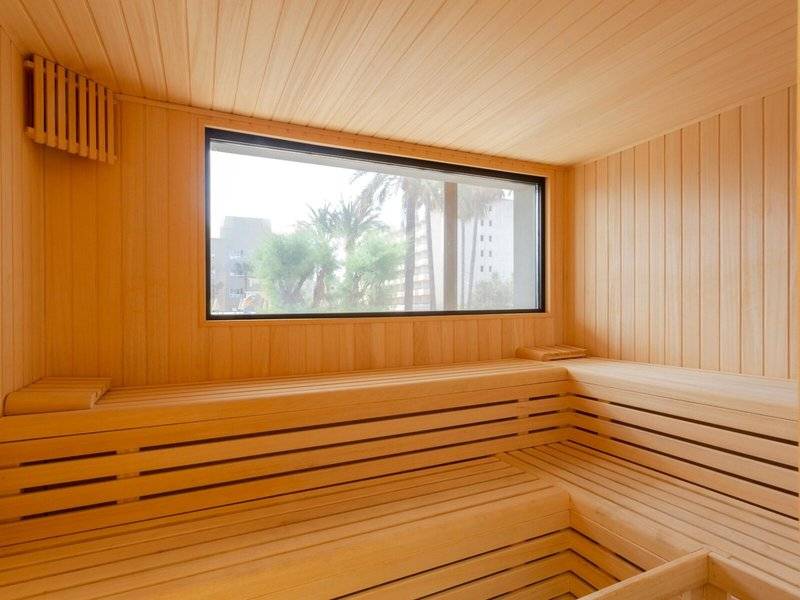 Innenansicht der Sauna im Aparthotel Marins Playa mit Holzwänden und einer großen Fensterscheibe.