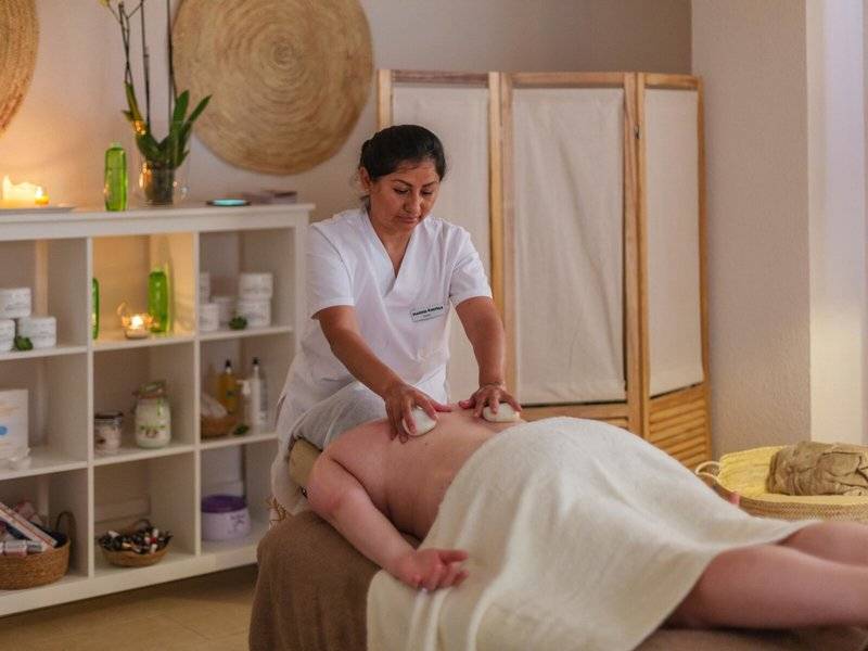 Eine Frau im weißen Dienstmädchenkostüm führt eine Massagebehandlung in einem Zimmer im Aparthotel Marins Playa durch.