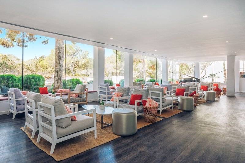 Loungebereich des Iberostar Cala Millor Hotels mit weißen Möbeln, roten Kissen und Glaswänden.
