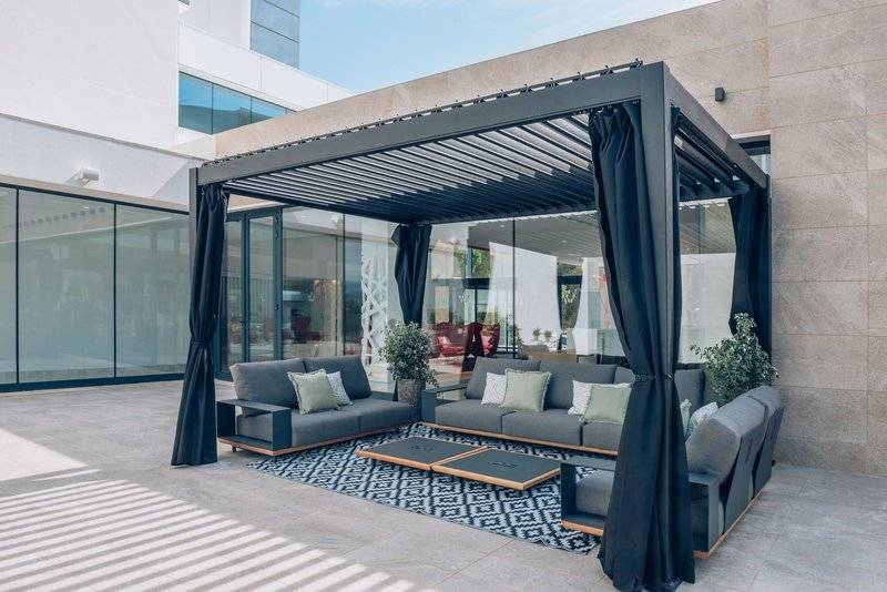 Außenlounge im Iberostar Cala Millor Hotel mit modernen Möbeln und schwarzen Vorhängen.