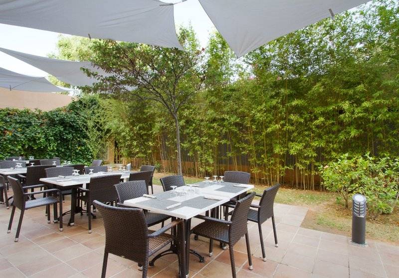 Foto von der Terrasse des Bakour Garbi Cala Millor Hotels mit Tischen und Stühle, umgeben von Bambusbepflanzung.