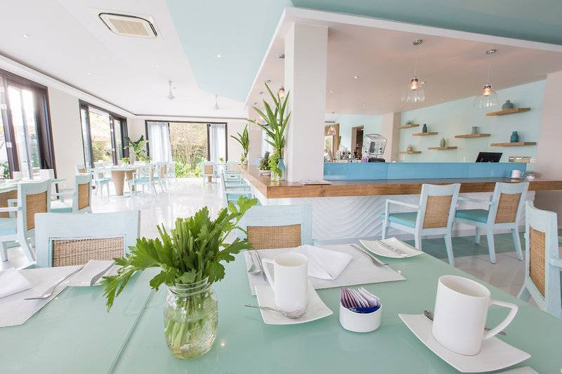 Innenansicht des Restaurants im TIA Wellness Resort mit blauen Tischen, Stühlen und einer Theke.