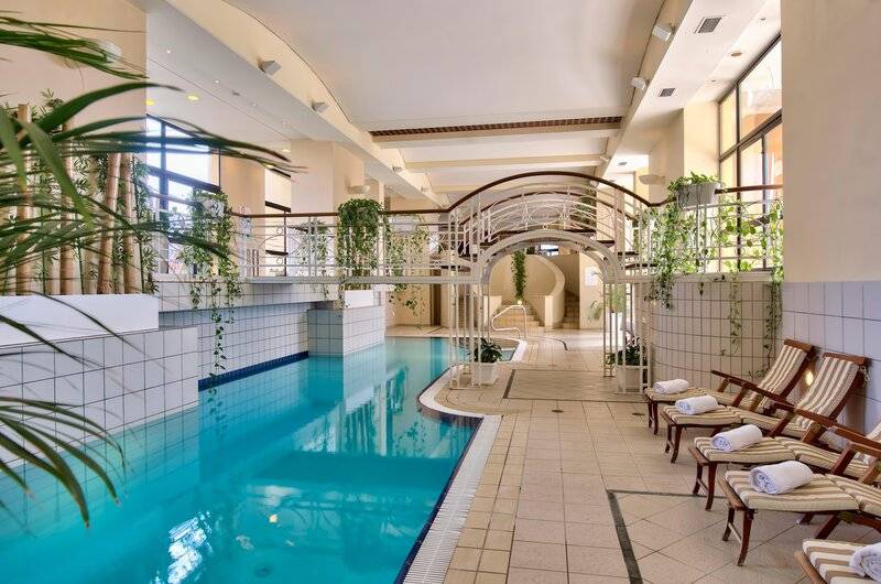 Innenpoolbereich des Corinthia St George's Bay Hotels mit Loungestühlen und Pflanzen.