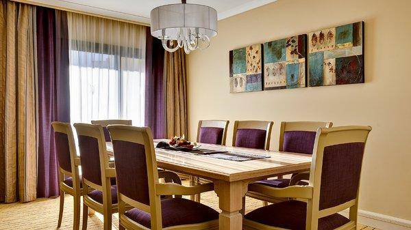 Speisesaal im Corinthia St George's Bay Hotel mit langem Tisch, Stühlen und Gemälden an der Wand.