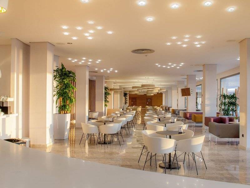Hotel RH Bayren & Spa mit geräumiger Lobby, runden Tischen und Stühlen, Pflanzen und moderner Inneneinrichtung.