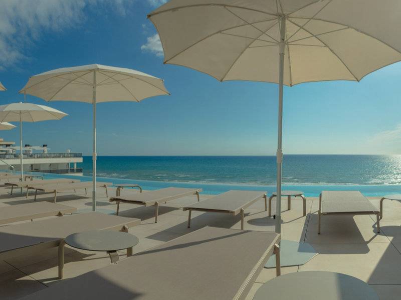 Terrasse des RH Bayren & Spa Hotels mit weißen Sonnenliegen und Sonnenschirmen am Meer