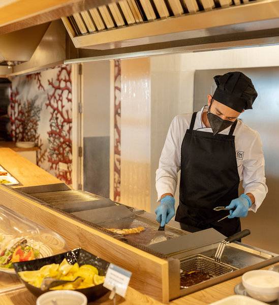 Koch im RH Bayren & Spa Hotel, der ein Gericht auf einem Grill vorbereitet.