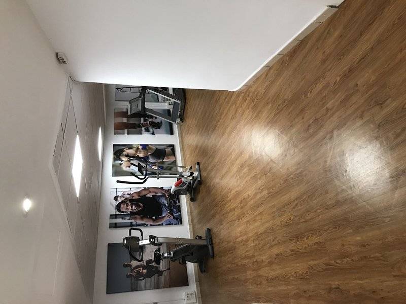Fitnessstudio mit Holzboden und Fitnessgeräten, darunter ein Laufband und ein Rudergerät.