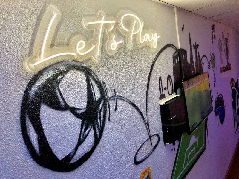 Eine Wand mit Graffiti, einem Fußball und der Beschriftung 'Let's Play'.