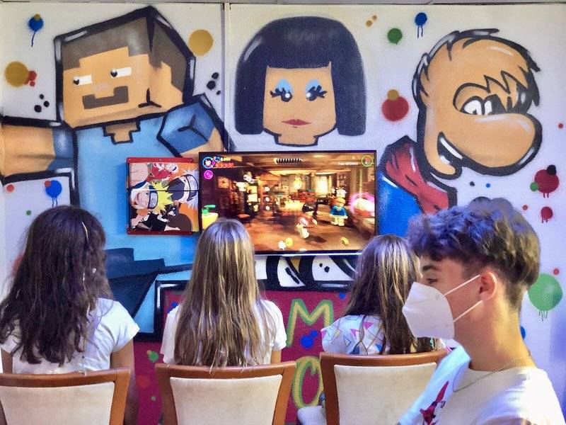 Kinder spielen ein Videospiel vor einer Wand mit bunten Graffiti im Principal Afilliated by RH Hotel.