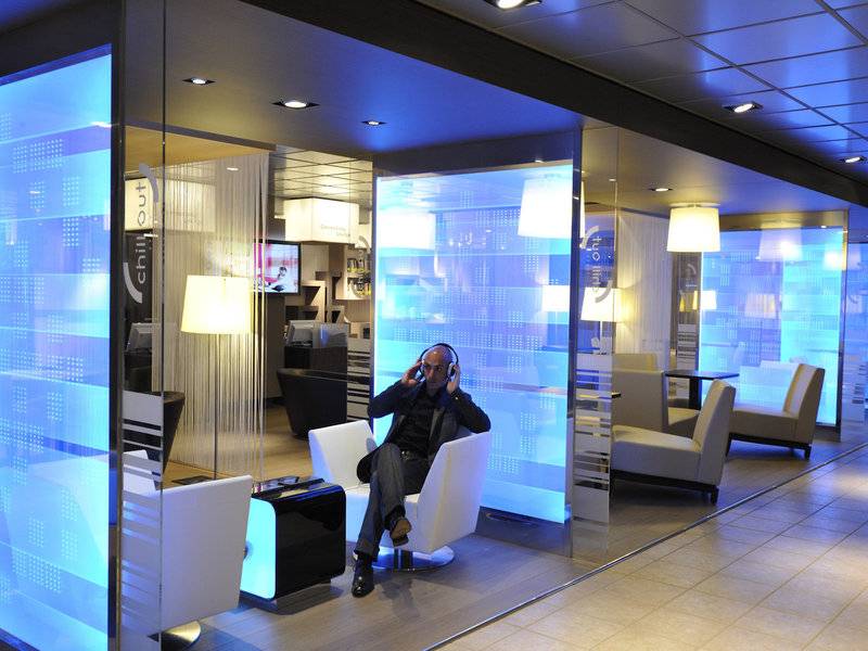 Mann mit Kopfhörern in einer Hotel-Lounge, mit blauen Lichtern und weißen Möbeln im Hintergrund.