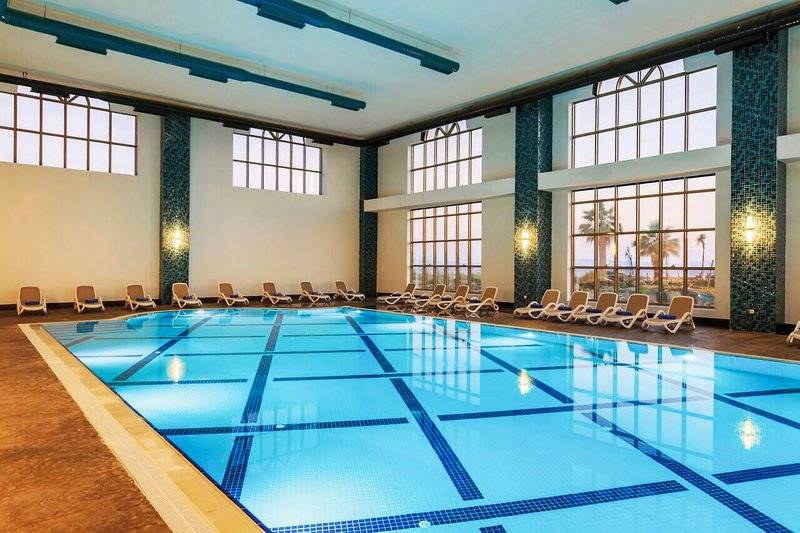 Ein großer Innenpool im Sunis Efes Royal Palace Resort & Spa mit Liegestühlen und großen Fenstern.