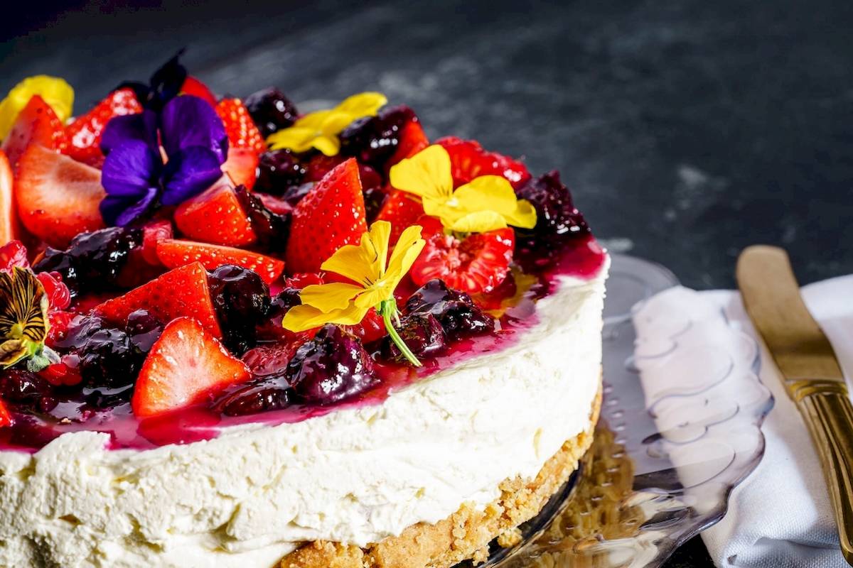 Ein Cremekuchen mit Früchten und Blumen darauf auf einem Glasteller.