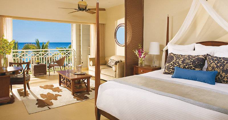 Gemütliche Suite im Secrets St. James Hotel mit Meerblick, Bett, Wohnzimmer und Balkon.