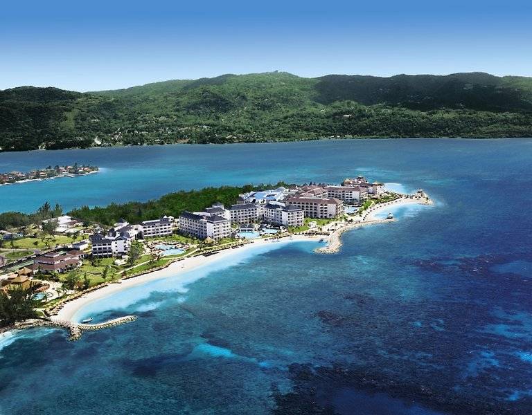 Luftaufnahme des Secrets St. James Hotel am Strand mit grünen Bergen im Hintergrund