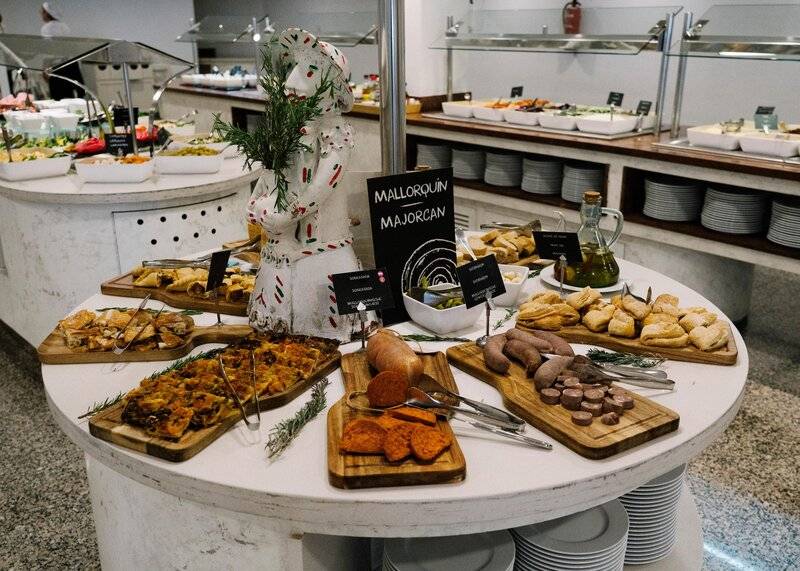 Buffettisch im Hotel ALUA Gran Camp de Mar mit verschiedenen Gerichten und einer beschrifteten Tafel.
