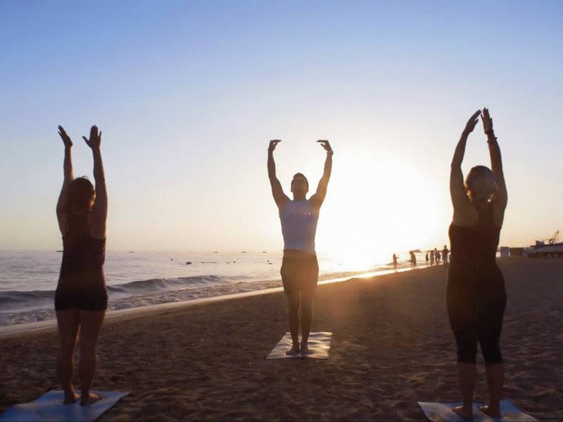 Drei Frauen praktizieren Yoga auf dem Strand vor dem TUI BLUE Side Hotel.